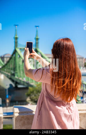 Schöne junge rothaarige Mädchen in baumwolle kleid Fotos ein Wahrzeichen Brücke an einem sonnigen Sommertag. Vertikale Foto Stockfoto