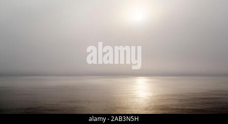 Morgen Sonnenschein glänzt durch Nebel an der Nordsee. Das Meer ist ruhig und die Sonne spiegelt Golden auf seiner Oberfläche. Stockfoto