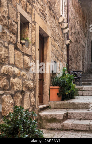 Schmalen alten mediterranen Straße mit Treppen in Korcula. Rauer Stein Häuser und Fassaden, grüne Pflanzen, Blumen in Dalmatien, Kroatien. Historischer Ort c Stockfoto