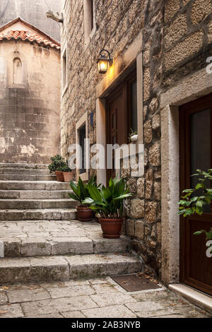 Korcula alten schmalen Mediterrane Straße mit Treppen. Rauer Stein Häuser und Fassaden, grüne Pflanzen, Blumen in Dalmatien, Kroatien. Historischer Ort crea Stockfoto