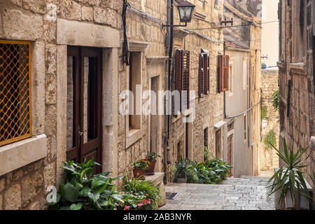 Korcula alten schmalen Mediterrane Straße mit Treppen. Rauer Stein Häuser, Fassaden mit Windows, grüne Pflanzen, Blumen in Dalmatien, Kroatien. Historische Stockfoto