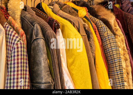 Seitenansicht der bunten gelb und braun getönte Vintage Kleidung, Jacken mit verschiedenen Mustern, Farben und Texturen hängen an einem Rack. Recylcing clothi Stockfoto