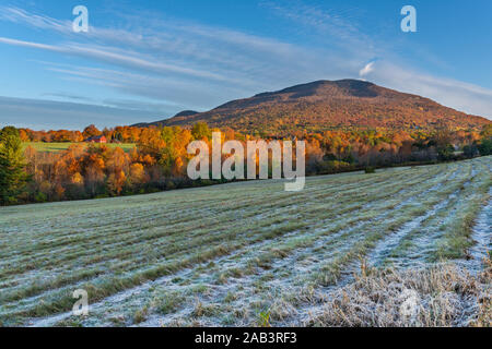 Herbstblick auf buntes Laub, Berge und Heufeld mit Frost und einem roten Bauernhaus in Manchester, Vermont. Stockfoto
