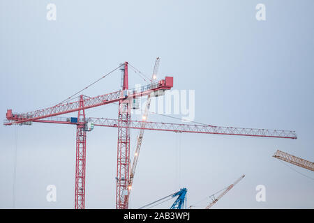 Gruppe von Kranen auf einer Baustelle, vor einem Gebäude montiert wird aus der Ferne während einem bewölkten Abend getroffen, unter einem grauen Himmel. Bild von Stockfoto