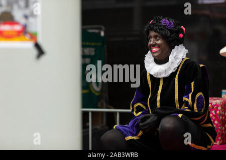 Eindhoven, Niederlande, 23. November 2019. Zwarte Piet das Tragen ihrer farbenfrohen Kostüm mit goldenen Details und lächelnd an der kleinen Kinder, welc Stockfoto