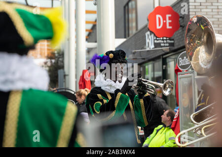 Eindhoven, Niederlande, 23. November 2019. Ein glückliches Piet Tragen seiner bunten grünen Kostüm in einer Blaskapelle spielen Sinterklaas Musik auf die Tr Stockfoto
