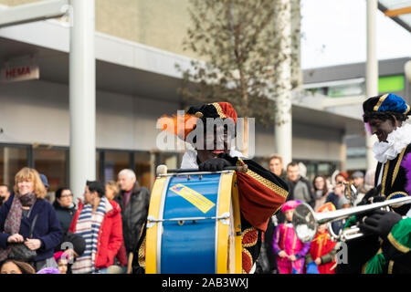 Eindhoven, Niederlande, 23. November 2019. Ein Piet Tragen seiner bunten Kostüm in einer Blaskapelle spielen Sinterklaas Musik auf die Base drum. Dut Stockfoto