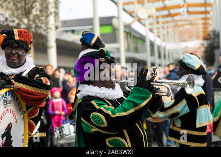 Eindhoven, Niederlande, 23. November 2019. Ein glückliches Piet Tragen seiner bunten Kostüm in einer Blaskapelle spielen Sinterklaas Musik. Niederländische traditio Stockfoto