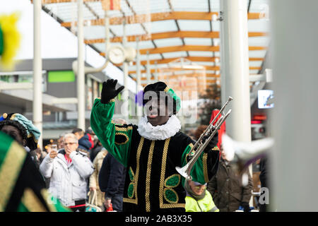 Eindhoven, Niederlande, 23. November 2019. Ein glückliches zwarte Piet Tragen seiner bunten grünen Kostüm und in einer Blaskapelle, seine Hände in die Stockfoto