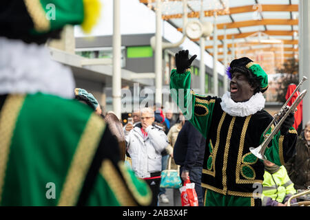 Eindhoven, Niederlande, 23. November 2019. Ein glückliches Piet Tragen seiner bunten grünen Kostüm und in einer Blaskapelle setzt seine Hände in die Luft wh Stockfoto