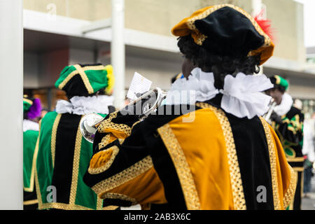 Eindhoven, Niederlande, 23. November 2019. Zwei glückliche Pieten tragen ihren bunten Kostüm in einer Blaskapelle spielen Sinterklaas Musik. Niederländische t Stockfoto