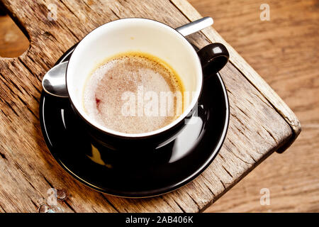 Eine halbvolle Tasse mit Espresso in einem alten Holzhocker | eine Hälfte - volle Tasse Espresso auf einem alten hölzernen Hocker | Stockfoto