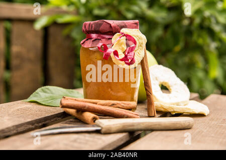 Ein Glas mit Apfelkonfitüre mit Zimtstangen in einer Obstkiste | ein Glas Apple Jam mit Zimtstangen auf einem Obst Kiste | Stockfoto