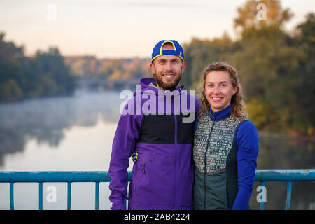 Junge lächelnde fitness Paar auf der Brücke stehen am Morgen Stockfoto