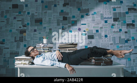 Erschöpft betonte Geschäftsfrau hinlegen und schlafen auf dem Schreibtisch, an der Wand mit finanzieller Berichte, die im Hintergrund Stockfoto