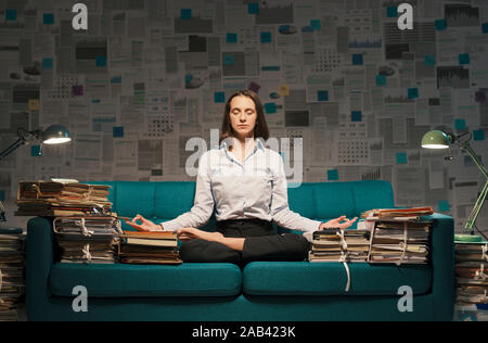 Corporate Geschäftsfrau im Lotus Position auf der Couch sitzen und die Praxis der Achtsamkeit Meditation konzentrieren und das Bewusstsein zu verbessern. Stockfoto