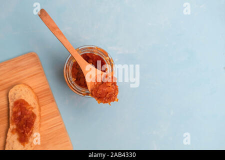 Leckere hausgemachte Karotte Marmelade im Glas mit Toast und Holzlöffel auf blauem Hintergrund Stockfoto