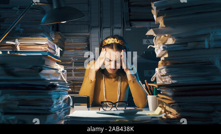 Erschöpft junge geschäftsfrau mit Kopf in den Händen mit Arbeit überlastet, sie ist gestresst und mit Kopfschmerzen. Stockfoto