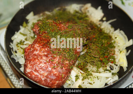 Rohes Hackfleisch mit Zwiebel und getrockneten Dill-Grüns mit Gewürzen in einer Bratpfanne in der heimischen Küche. Kochvorgang. Stockfoto