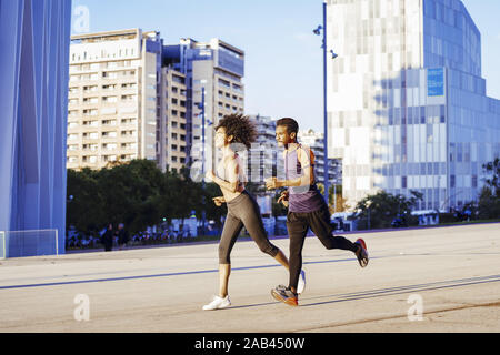 Schön und sportlich Latin Frau und sportliche schwarze Mann zusammen bei Sonnenuntergang in der Stadt mit Gebäuden im Hintergrund. urban Sport w Stockfoto