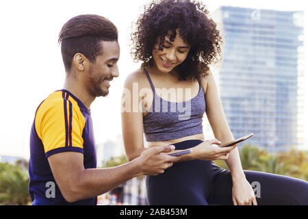 Porträt einer athletischen Latin Frau und Mann in Schwarz über ihre Mobiltelefone während der Rest im Training, Technik im Sport und gesunde Lebensweise con Stockfoto