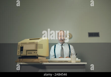 Traurig senior Geschäftsmanns, der mit einem veralteten Computer auf einem kleinen Schreibtisch, Er ist traurig und enttäuscht. Stockfoto