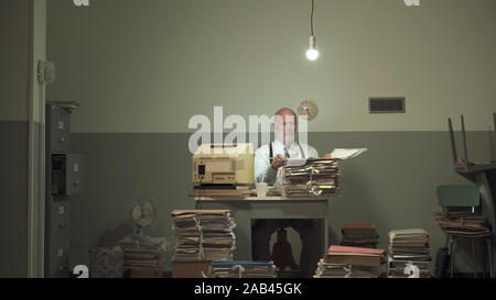 Frustriert Vintage Style Geschäftsmanns, der sich in einem heruntergekommenen Büro, er ist mit papework überlastet Stockfoto