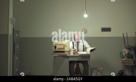 Traurig Vintage Style Geschäftsmanns, der in einem kleinen heruntergekommenen Büro mit einem alten Computer und billige Möbel, er fühlt sich unglücklich und enttäuscht Stockfoto