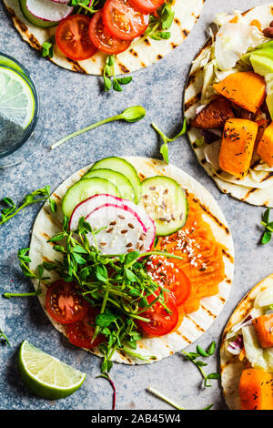 Öffnen Sie vegan Tortilla Wraps mit süssen Kartoffeln, Bohnen, Avocado, Tomaten, Kürbis und Pflanzgut auf grauem Hintergrund, Flach, Ansicht von oben. Gesund vegan f Stockfoto