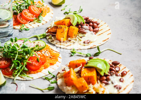 Öffnen Sie vegan Tortilla Wraps mit süssen Kartoffeln, Bohnen, Avocado, Tomaten, Kürbis und Pflanzgut auf grauem Hintergrund, flach. Gesunde vegane Ernährung anhand von quantitativen Simulatio Stockfoto