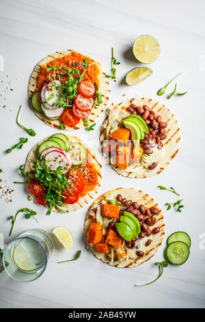 Öffnen Sie vegan Tortilla Wraps mit süssen Kartoffeln, Bohnen, Avocado, Tomaten, Kürbis- und Pflanzgut auf einem weißen Hintergrund, Ansicht von oben, flach. Gesund vegan Stockfoto