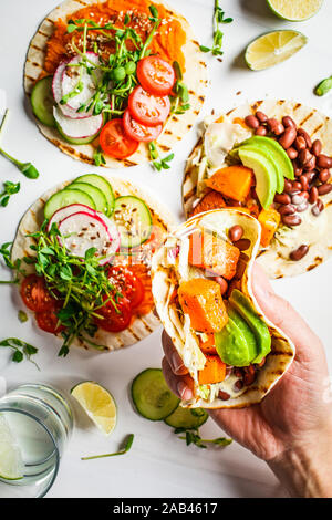 Öffnen Sie vegan Tortilla Wraps mit süssen Kartoffeln, Bohnen, Avocado, Tomaten, Kürbis- und Pflanzgut auf einem weißen Hintergrund, Ansicht von oben, flach. Gesund vegan Stockfoto