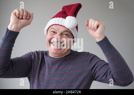 Happy senior Hispanic Mann Gefühle zum Ausdruck zu bringen gute Weihnachten. Studio Portrait von überrascht Vater Weihnachtsmann trägt Hut und blauen Pullover. Positive Stockfoto