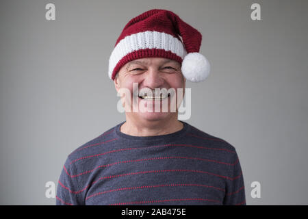Happy senior Hispanic Mann Gefühle zum Ausdruck zu bringen gute Weihnachten. Studio Portrait von überrascht Vater Weihnachtsmann trägt Hut und blauen Pullover. Positive Stockfoto