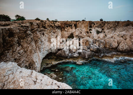 Eine blaue Lagune in Cape Greco, Zypern. Das Wasser hat viele Schattierungen von Blau. Kristallklares Wasser. Scharfe Felsen aus dem Meer. Ruhige Oberfläche der se Stockfoto