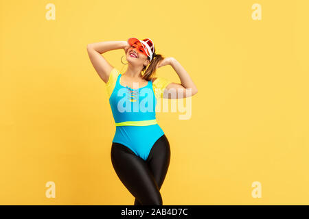Junge kaukasier plus Schulung die Größe der weiblichen Modell auf gelben Hintergrund. Copyspace. Konzept für Sport, gesunder Lebensstil, Körper positive, Mode, Style. Stilvolle Frau kühlen, Ruhen und lächelnd. Stockfoto