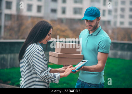 Dunkelhaarige Frau, die in der Nähe von Delivery Man Holding boxen Stockfoto