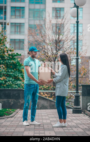 Fröhliche delivery man vorbei an Bag zu den ständigen Kunden Stockfoto