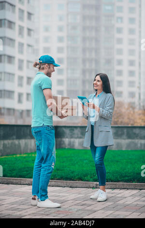 Lieferung Mann mit Kappe Holding boxen, während in der Nähe von Kunden stehen Stockfoto