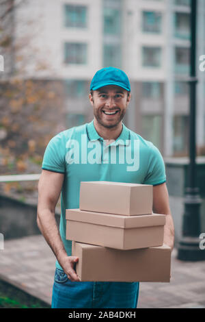 Lächelnd Lieferung Mann mit Kappe Holding boxen für Clients Stockfoto