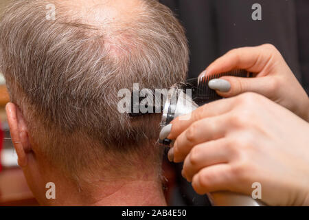 Frau Friseur schneidet die Haare des Mannes mit elektrischer Haarschneider Trimmer. Selektiver Fokus Stockfoto