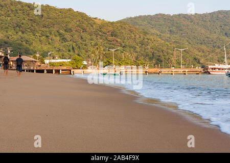 Ilha Grande, Brasilien. 24. Dezember, 2012. Menschen gehen auf die Küste in Richtung Estacao Santorini Santorini (Ferry Terminal) und Cais Turistico da Vila do Santorini (touristische Pier von Santorini Dorf), Sandstrand während der sonnigen Morgen gesehen, Ilha Grande, die Gemeinde von Angra dos Reis, Bundesstaat Rio de Janeiro, Brasilien. Am 5. Juli 2019, Ilha Grande wurde von der UNESCO als Weltkulturerbe eingetragen. Stockfoto