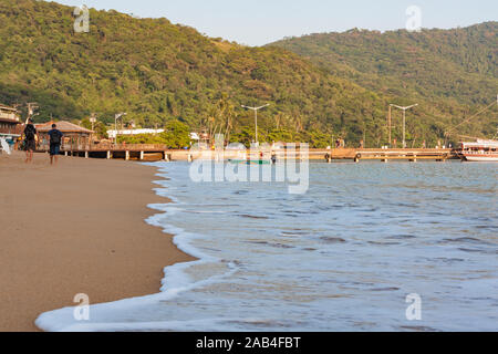 Ilha Grande, Brasilien. 24. Dezember, 2012. Menschen gehen auf die Küste in Richtung Estacao Santorini Santorini (Ferry Terminal) und Cais Turistico da Vila do Santorini (touristische Pier von Santorini Dorf) wie Meerwasser Ansatz und Spill auf Sandstrand, während der sonnigen Morgen gesehen, Ilha Grande, die Gemeinde von Angra dos Reis, Bundesstaat Rio de Janeiro, Brasilien. Am 5. Juli 2019, Ilha Grande wurde von der UNESCO als Weltkulturerbe eingetragen. Stockfoto