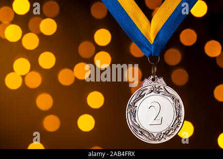 Silber zweiten Platz Vizemeister Meisterschaft Medaillon auf ein Band hängt über einem gelben Hintergrund mit bunten orange bokeh Wirkung der Partei leuchtet Stockfoto