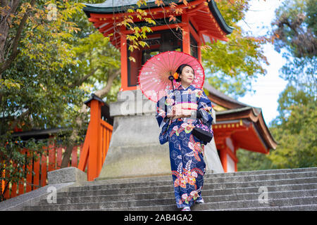 Geishas Mädchen mit japanischen kimono unter roten Holz- Tori Gate bei Fushimi Inari Schrein in Kyoto, Kimono ist ein traditionelles japanisches Gewand. Das Wort " Stockfoto