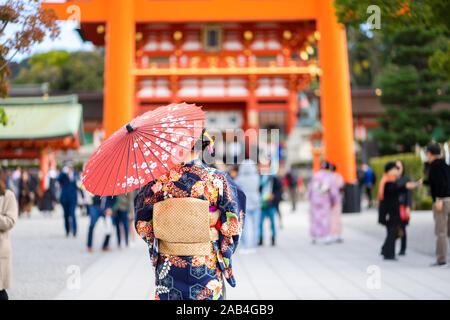 Geishas Mädchen mit japanischen kimono unter roten Holz- Tori Gate bei Fushimi Inari Schrein in Kyoto, Kimono ist ein traditionelles japanisches Gewand. Das Wort " Stockfoto