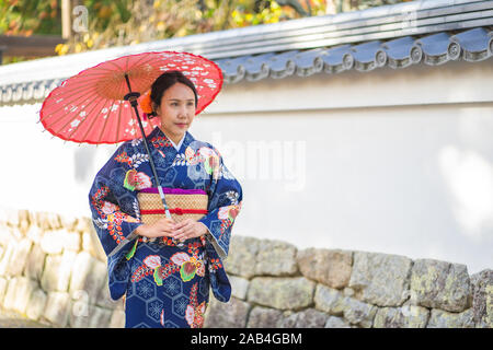 Geishas Mädchen mit japanischen kimono unter roten Holz- Tori Gate bei Fushimi Inari Schrein in Kyoto, Kimono ist ein traditionelles japanisches Gewand. Das Wort " Stockfoto