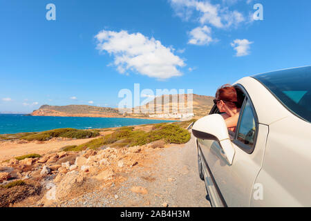 Gerne reife Frau mit Sonnenbrille im Auto auf hellen, sonnigen Tag in der Nähe von Ocean. Die Frau blickt zurück in Richtung Meer. Kopieren Sie Platz. Stockfoto