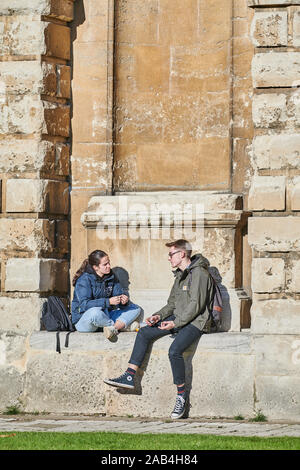 Ein paar Studenten, eine Frau, die anderen männlichen, sitzen auf einem Felsvorsprung außerhalb des Radcliffe Camera Bodleian Library an der Universität von Oxford, En Stockfoto