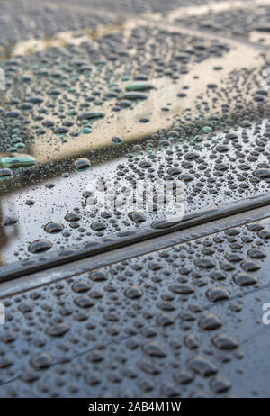 Regentropfen auf glänzenden schwarzen Oberfläche mit Schiebedach Auto auf dem Dach gebündelt - nach einem Regenschauer, und reflektierenden blaue Himmel und die umliegenden Gebäude. Stockfoto